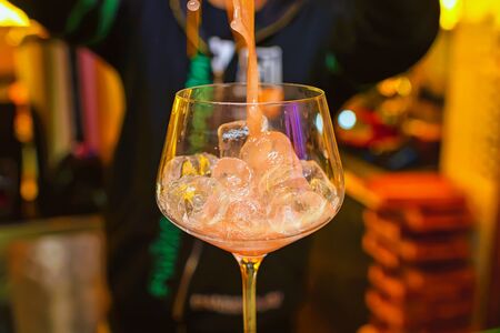 Preparation of a cocktail by a bartender from ice cubes of alcohol and juice. The flow of liquid flows into a glass of ice.の写真素材
