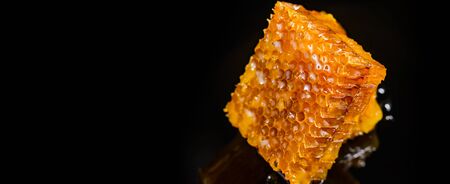 Honey close-up. Amber sweet honey in honeycomb. Square cut piece of honeycomb with honey on a black...