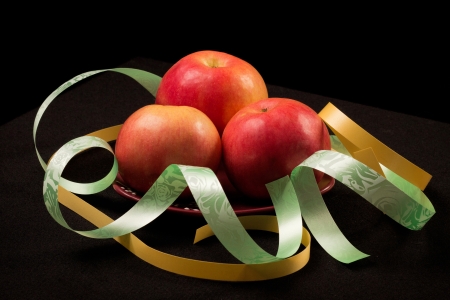 Red apples on a black background with color ribbonsの写真素材