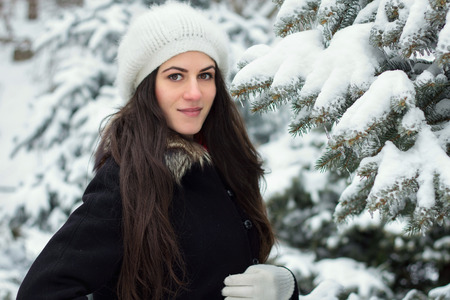 Cheerful young woman standing outside near a snow covered branch of a fir treeの写真素材