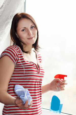 Careful brunette young girl washes and cleans a windowの写真素材
