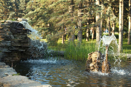 Beautiful pond with fountain in park made in handmade of stones and evergreen plant