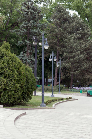 Views of a well-equipped city park with classical lanterns and sound speakers, benches and large trees. Here people rest and walkの写真素材