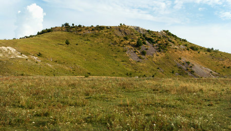 Beautyful view from below of the hill and clouds on a sunny summer's day. Grass, trees and many stones grow on hill. Small stones pour down in non-weather conditionsの写真素材