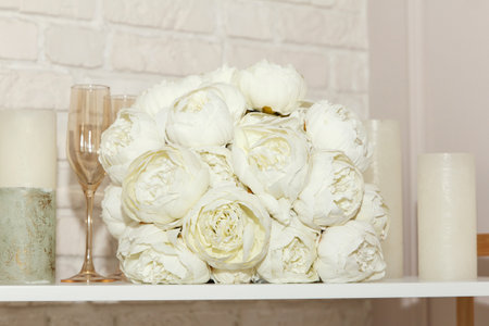 A wedding white bouquet of peonies, glasses and white candles lie on a shelf. Beautiful wedding set for bride. beautiful background.の写真素材