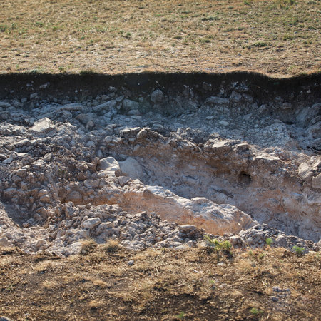 Exposed scientific work archaeological dig site showing soil layers and chalky surface, daylight...