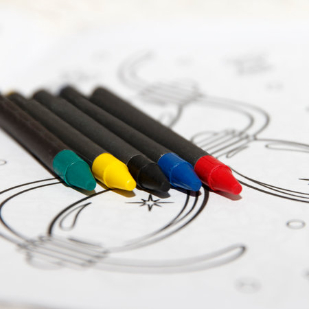 Coloring markers arranged on a table next to coloring pages. Markers are in red, blue, green, and yellow. Pages feature simple line drawingsの写真素材