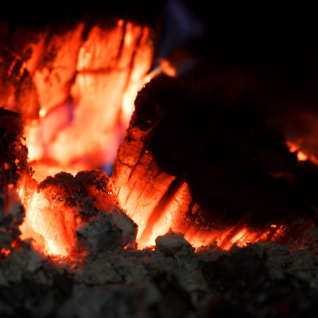 Close-up of glowing embers and burning wood in a fireplace. Scene captures the warmth and light of a...