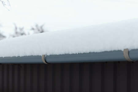 Snow-covered roof edge with a gray gutter. Scene captures a winter atmosphere with a soft layer of snow resting on structureの写真素材