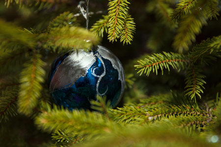 A blue Christmas ornament hangs among green pine branches. Ornament features a design resembling the Earth, symbolizing holiday spirit and natureの写真素材