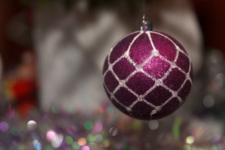 A close-up of a shiny purple Christmas ornament with a white geometric pattern, hanging against a blurred festive backgroundの写真素材