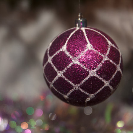 A close-up of a shiny purple Christmas ornament with a white geometric pattern, hanging against a blurred festive backgroundの写真素材