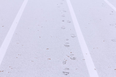 Footprints on a snowy track with white lines. Scene captures a winter landscape, emphasizing cold...