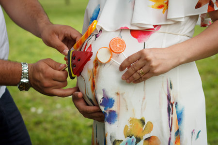 A close-up of an expectant couple's hands. A man holds colorful lollipops to his partner's pregnant...