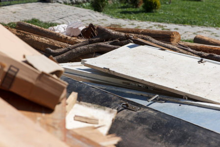 Close-up of a messy pile of renovation debris outdoors. Old white doors, wooden logs, and cardboard...