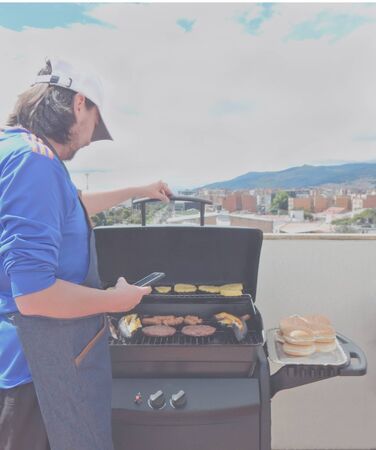 man cooking food on barbecue grill outdoors with city blurred backgroundの写真素材