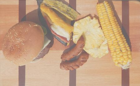 homemade hamburger with corn, banana, pineapple and sausages spread out on a wooden boardの写真素材