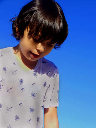 kid in a white shirt looking down on a blue backgroundの写真素材