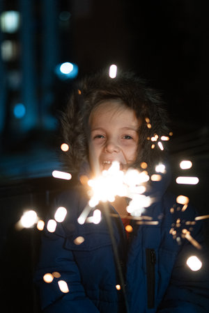 Boy holding sparklers in front of high-rise buildings on a winter night