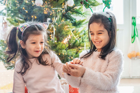 Children lighting sparklers near a festive Christmas tree. Happy moments of anticipation for...