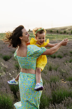 Mother and daughter enjoying a joyful picnic, running in the park, playing by the lake, and having fun in a lavender field. Bright outfits, summer vibes, and heartfelt family moments.の写真素材