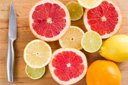 Sliced fresh citrus (lemons, limes, grapefruits, oranges) on a wooden cutting board with a metal knife, top viewの写真素材