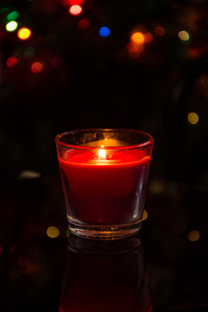 A lit red candle in a dark room with bokeh lights in the backgroundの写真素材
