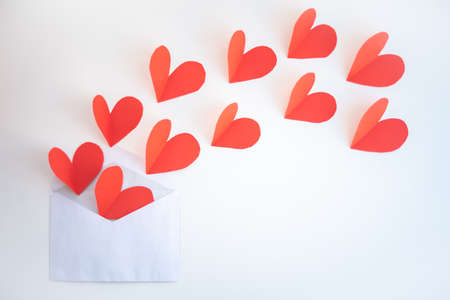 Red paper hearts fly out of an envelope on a white background.