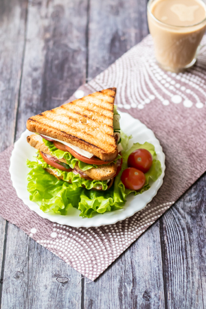 Sandwich with cheese, tomato, cucumber, sausage and lettuce on a wooden background. Vertical orientationの写真素材