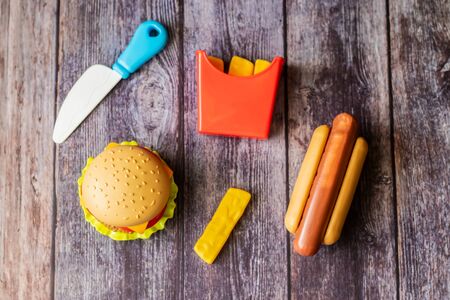 Plastic burger, salad, tomato, frying potatoes with hot dog on a wooden background. Horizontal orientation. Children's toy. The concept of harmful artificial food. Plastic Not organic. Not healthy.の写真素材