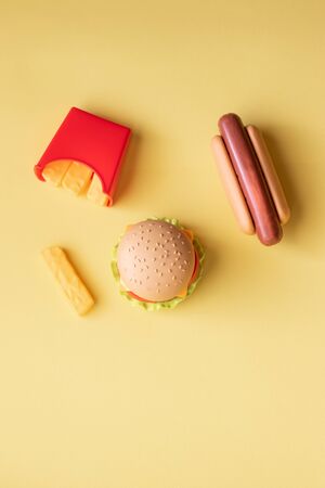 Plastic burger, salad, tomato, frying potatoes with a hot dog on a yellow background. Vertical orientation. Children's toy. The concept of harmful artificial food. Plastic Not organic. Not healthy.の写真素材