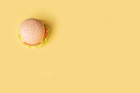 Plastic burger, salad, tomato, on a yellow background. Vertical orientation. Children's toy. The concept of harmful artificial food. Plastic Not organic. Not healthy. Copy spaceの写真素材