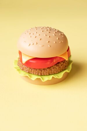 Plastic burger, salad, tomato, on a yellow background. Vertical orientation. Children's toy. The concept of harmful artificial food. Plastic Not organic. Not healthy.の写真素材