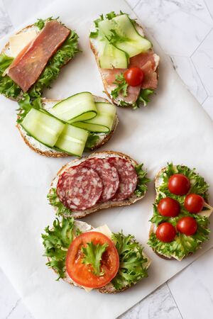 Fresh sandwiches with sausage, cheese, bacon, tomatoes, lettuce, cucumbers on a light background. Vertical orientationの写真素材
