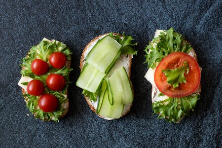 Fresh sandwiches with sausage, cheese, bacon, tomatoes, lettuce, cucumbers on a dark background. Horizontal orientationの写真素材