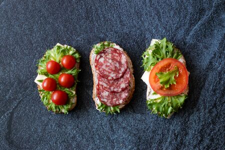Fresh sandwiches with sausage, cheese, bacon, tomatoes, lettuce, cucumbers on a dark background. Horizontal orientationの写真素材