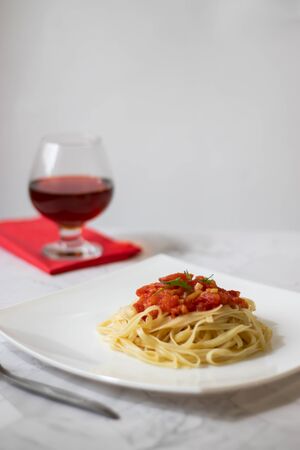 Pasta with fresh tomatoes, cooked with olive oil and garlic on a light background and a white square plate. Italian food. Vertical orientationの写真素材