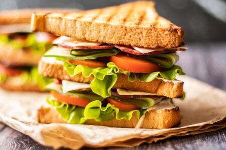 Sandwich with cheese, tomato, cucumber, sausage and salad on wooden background. Horizontal orientationの写真素材