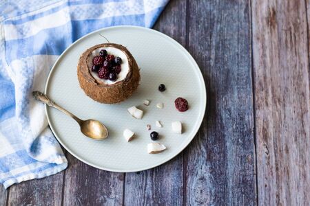 Berry dessert with yogurt in a cup of coconut on a wooden background. Blackberries, raspberries,...