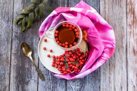Hot healing tea, mountain ash tea. Reduces the level of harmful cholesterol in the blood, strengthens blood vessels. healing drink on a wooden background with a pink napkinの写真素材