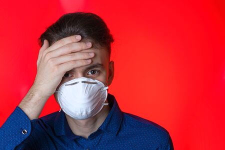Virus-sick young man on self-isolation in a protective mask. Protects itself and others from the spread of coronavirus, on a red backgroundの写真素材
