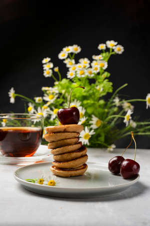 A trendy homemade breakfast with tiny pancakes close-up. Mini pancakes, cherries, tea on the table.の写真素材