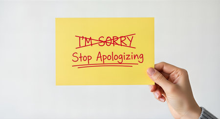 Hand displays a yellow card with bold red text stating "Stop Apologizing," symbolizing the importance of forgiveness and resolving conflicts in relationshipsの素材