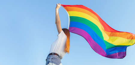 Woman holding the lisbian Rainbow lgbt Flag over blue sky outdoors. Happiness freedom and love...