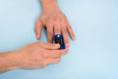 Human hand pulse oximeter used to measure pulse rate and oxygen levels with medical blue background with copy space. Male hand measures heart rate with heart rate monitor top view, Medical conceptの写真素材