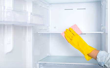 A woman's hand in a yellow rubber protective glove and a pink sponge washes and cleans the...