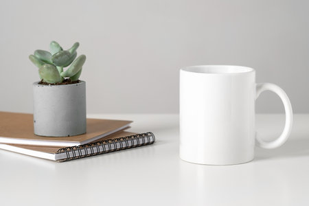 White mug mockup on table in minimalist interior, business concept, succulent and notepads. Template, layout for your design, advertising, logo with copy space. Cup on light gray background.の写真素材