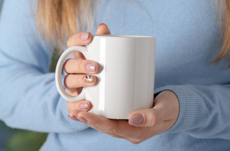 Female hands hold mock up white empty mug, cup for your design and logo closeup. Template blank for promotional text message or promotional content.の写真素材