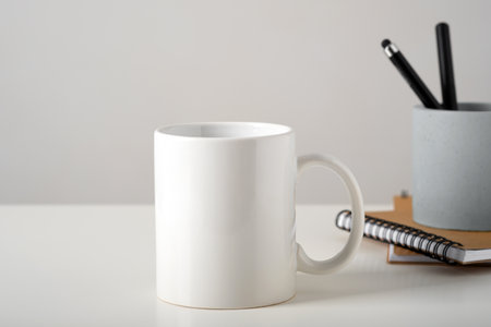 Mockup of a white mug on a table in a minimalist interior, business stationery and notepads. Template, layout for your design, advertising, logo with copy space. Cup on light gray background.の写真素材