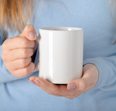 Female hands hold mock up white empty mug, cup for your design and logo closeup. Template blank for promotional text message or promotional contentの写真素材